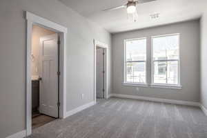 Unfurnished bedroom with ensuite bathroom, carpet flooring, and ceiling fan