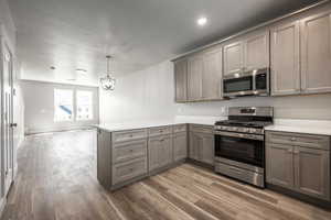 Kitchen with hanging light fixtures, hardwood / wood-style floors, stainless steel appliances, a textured ceiling, and kitchen peninsula