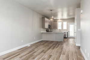 Kitchen with appliances with stainless steel finishes, wood-type flooring, gray cabinetry, a notable chandelier, and kitchen peninsula