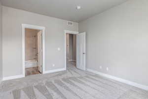 Unfurnished bedroom featuring ensuite bath and light carpet