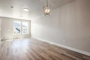 Empty room with hardwood / wood-style flooring, a notable chandelier, and a textured ceiling