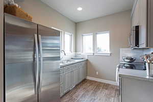 Kitchen featuring stainless steel appliances, sink, decorative backsplash, and gray cabinetry