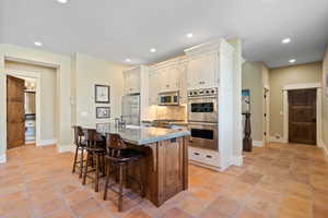 Kitchen featuring light tile patterned floors, tasteful backsplash, a kitchen bar, stainless steel appliances, and light stone counters