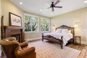 Bedroom with ceiling fan, a tiled fireplace, and hardwood / wood-style flooring