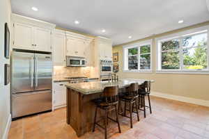 Kitchen with backsplash, an island with sink, a breakfast bar, stainless steel appliances, and light tile patterned flooring