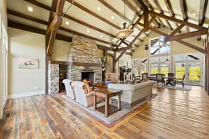 Living room with a fireplace, beamed ceiling, wood-type flooring, and high vaulted ceiling