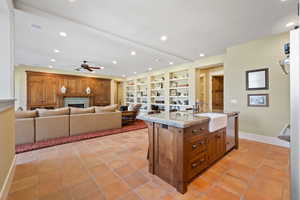 Kitchen with light tile patterned floors, a tiled fireplace, dishwasher, ceiling fan, and a kitchen island with sink