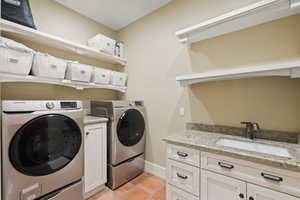 Washroom with cabinets, washer and clothes dryer, sink, and light tile patterned floors