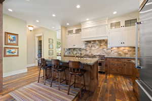 Kitchen with dark hardwood / wood-style floors, backsplash, a kitchen island with sink, light stone counters, and premium appliances