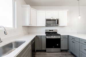 Kitchen with sink, appliances with stainless steel finishes, gray cabinets, pendant lighting, and white cabinets