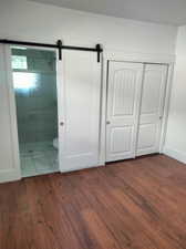 Interior space featuring dark wood-type flooring, a closet, a barn door, and ensuite bathroom