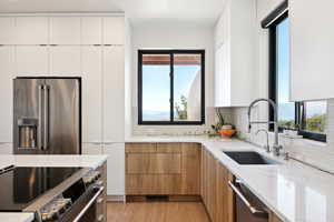 Kitchen featuring backsplash, appliances with stainless steel finishes, light hardwood / wood-style floors, sink, and white cabinetry