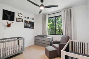 Bedroom featuring light hardwood / wood-style flooring, a nursery area, and ceiling fan