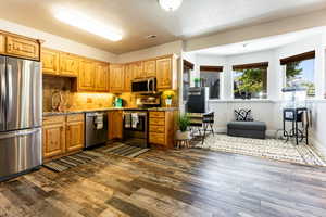 Kitchen with backsplash, stainless steel appliances, light stone counters and sink.