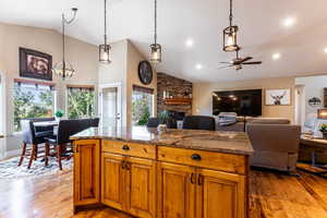 Kitchen featuring ceiling fan with notable chandelier, a fireplace, a center island, light wood-type flooring, and stone counters