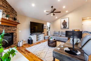 Living room with light wood-type flooring, high vaulted ceiling, ceiling fan, and a stone fireplace