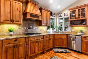 Kitchen featuring custom range hood, appliances with stainless steel finishes, light hardwood / wood-style floors, sink, and lofted ceiling