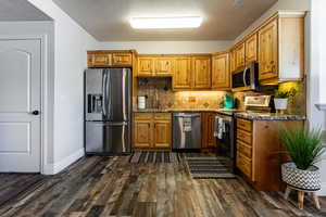 Kitchen with appliances with stainless steel finishes, sink, dark stone counters, and decorative backsplash