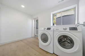 Clothes washing area with washing machine and clothes dryer and light hardwood / wood-style floors