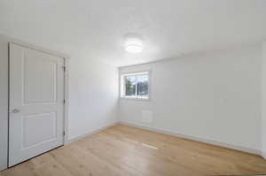 Spare room with a textured ceiling and light hardwood / wood-style floors