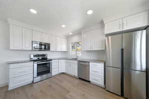 Kitchen with light wood-type flooring, appliances with stainless steel finishes, and white cabinets