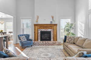 Living room featuring an inviting chandelier, light hardwood / wood-style flooring, a towering ceiling, and a fireplace