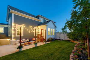 Back house at dusk featuring outdoor lounge area, a patio area, and a yard