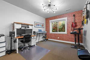 Office featuring carpet floors, brick wall, a notable chandelier, and a textured ceiling