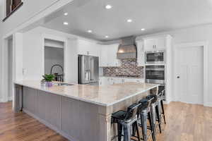 Kitchen with white cabinets, stainless steel appliances, custom range hood, a breakfast bar area, and light stone countertops