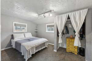 Bedroom featuring dark carpet, track lighting, and a textured ceiling