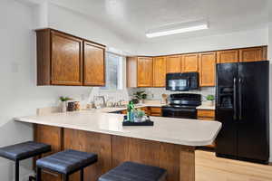 Kitchen with light wood-type flooring, black appliances, a breakfast bar area, and kitchen peninsula