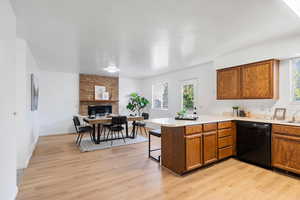 Kitchen with black dishwasher, light hardwood / wood-style flooring, kitchen peninsula, and a fireplace