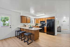 Kitchen featuring black appliances, a kitchen breakfast bar, kitchen peninsula, and light hardwood / wood-style flooring