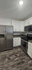 Kitchen featuring appliances with stainless steel finishes, white cabinetry, a textured ceiling, and dark hardwood / wood-style floors