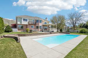 Rear view of property featuring a balcony, a chimney, fence, a fenced in pool, and brick siding