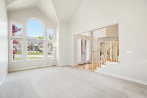 Spare room with high vaulted ceiling, carpet flooring, stairs, and plenty of natural light