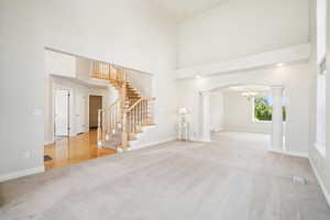 Carpeted foyer entrance with stairs, a high ceiling, arched walkways, baseboards, and decorative columns