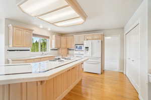 Kitchen featuring a sink, tile countertops, light brown cabinetry, white appliances, and light wood finished floors