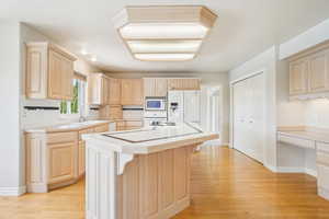 Kitchen featuring light brown cabinetry, light countertops, white appliances, and a kitchen island