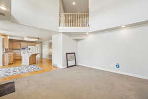Unfurnished living room with baseboards, visible vents, a towering ceiling, and light colored carpet