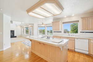 Kitchen featuring open floor plan, light brown cabinets, a sink, and white appliances