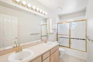 Bathroom featuring double vanity, toilet, enclosed tub / shower combo, and a sink