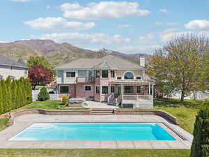 Back of house featuring a fenced backyard, brick siding, a lawn, a hot tub, and a balcony