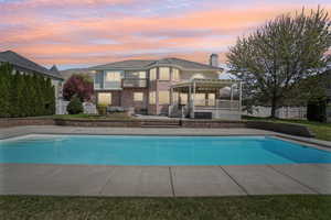 Pool at dusk with a pergola, fence, a patio area, a deck, and an outdoor pool