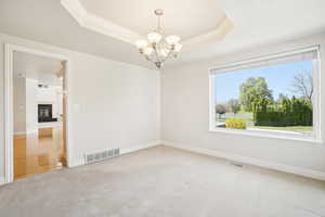 Spare room featuring visible vents, an inviting chandelier, a raised ceiling, and light colored carpet