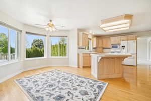 Kitchen with white appliances, a kitchen island, light brown cabinets, light countertops, and a breakfast bar