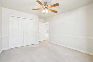 Unfurnished bedroom featuring a closet, baseboards, ceiling fan, and light colored carpet