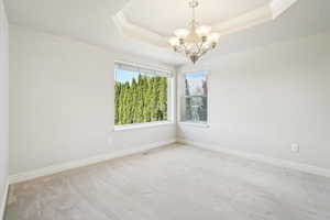 Carpeted empty room featuring a chandelier, baseboards, ornamental molding, and a tray ceiling