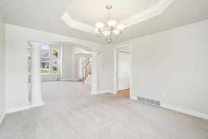 Unfurnished dining area with a chandelier, arched walkways, a tray ceiling, visible vents, and ornate columns