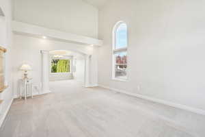 Spare room featuring a high ceiling, light carpet, arched walkways, baseboards, and decorative columns